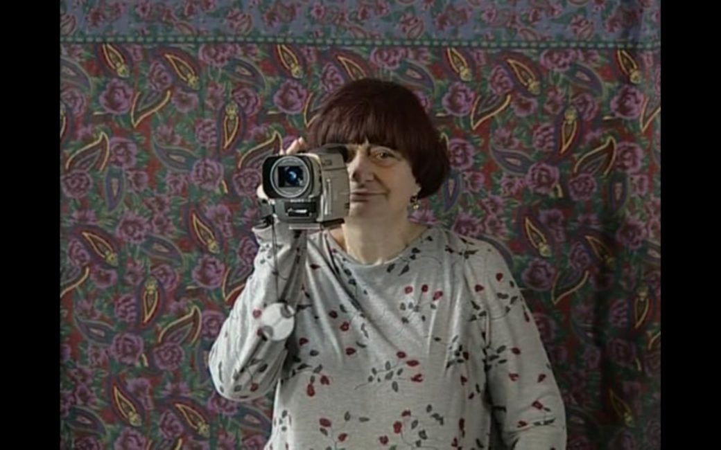 La réalisatrice pose pour un portrait. Elle tient sa caméra numérique de sa main droite et elle a son œil collé à l’œilleton.